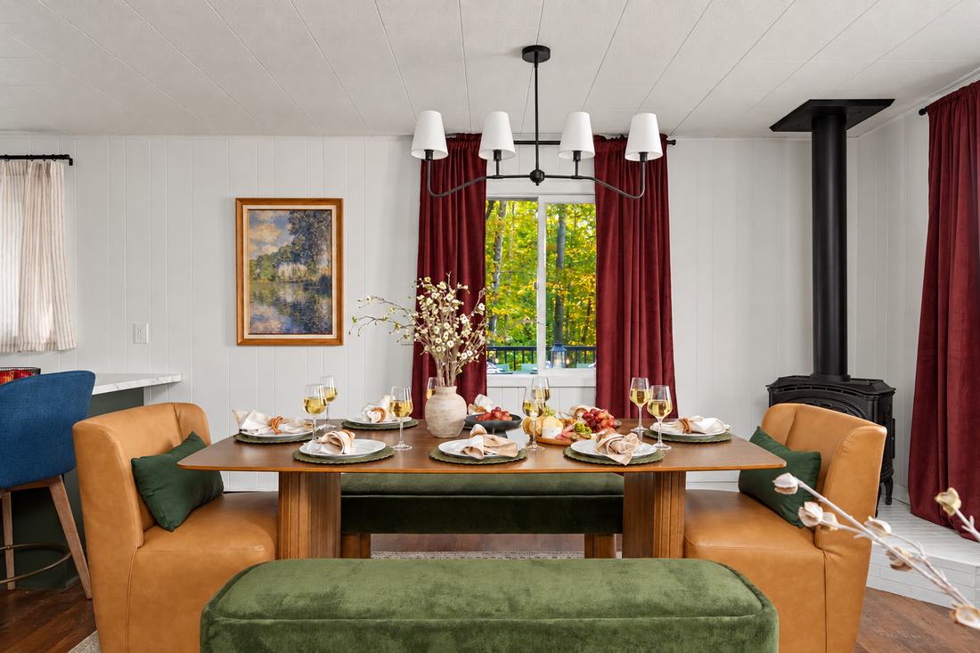 Dining table set for dinner with leather chairs, green velvet benches and a wood stove