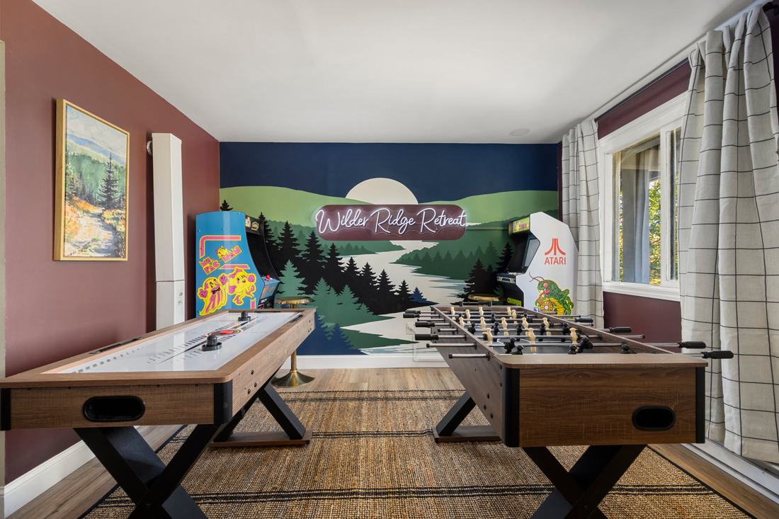 Game room with air hockey, foosball, two arcade cabinets and the Wilder Ridge Retreat neon sign on a lake mural
